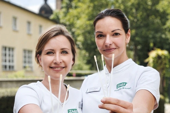 Zwei Mitarbeiterinnen vom Lebensretter Stützpunkt Zags in Dresden halten drei Wattestäbchen in der Hand.